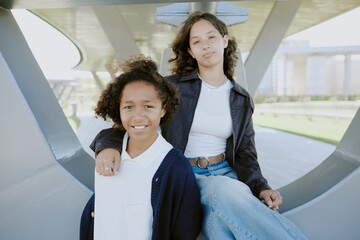 Portrait of best friend teens dressed in casual clothes sitting on metal construction while posing...