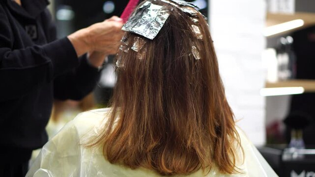 Beauty salon. Professional stylist combs client hair after applying paint with brush. hair coloring in hairdressing salon. Close-up of hairdresser in beauty salon. Painting on foil