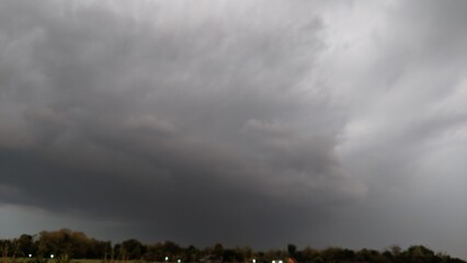 A menacing storm cloud looms over a landscape, casting a dark shadow. The cloud's base is low and ominous, suggesting the potential for severe weather.