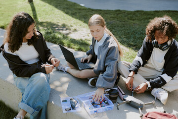 Biracial teen friends in casual clothes sitting on cement making drone together while using laptop...