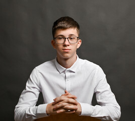 A young guy in a white shirt is sitting at a desk and clasping his hands tightly.