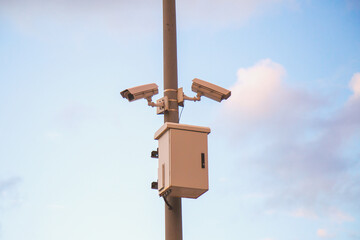 two street CCTV cameras hang on a pole against the backdrop of a beautiful sunset sky