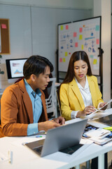 Two asian businesspeople are working together in office meeting, using laptop and discussing project strategy