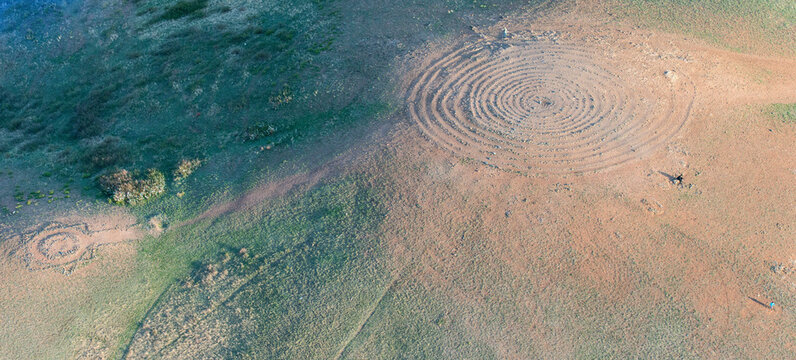 Aerial view of circular patterns in green grass fields at the archaeological site of Arkaim, Chelyabinsk Oblast, Russia.