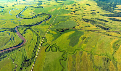 Aerial view of meandering river through lush green fields and textured wetlands, Omsk Oblast, Russia.