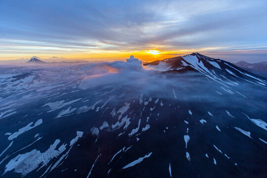 Aerial view of mutnovsky volcano at sunset surrounded by snow and clouds, kamchatka peninsula, russia.