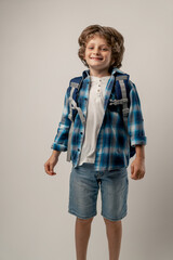 in a photo studio on a white background stands a smiling schoolboy in a white sweater and a blue checkered shirt with briefcase on his back jumping on the spot