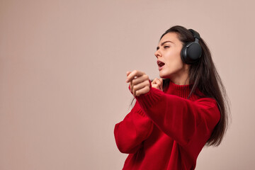 Happy excited woman wearing red sweater and headphones enjoying listening music and dancing, copy space