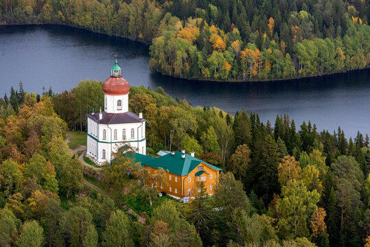 Aerial view of a picturesque church by a tranquil lake surrounded by lush autumn forest, Onega Bay, Karelia republic, Russia.