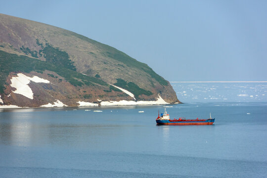 Aerial view of a serene coastal landscape with a ship on calm waters and snow-capped mountains, Beringovsky, Russia.