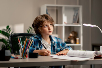 in the children's room a schoolboy in a white sweater and a blue checkered shirt at a desk doing...