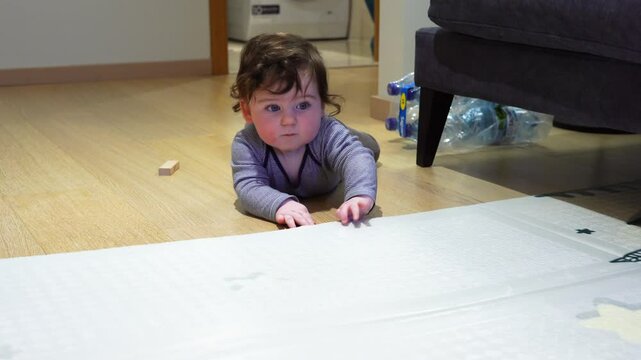 Seven month old boy with very thick dark hair lies on the floor and plays with a rug (193)