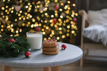 Glass of milk and cookies for Santa Claus on the table near the Christmas tree