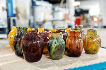 Many colorful glass vases at glass blowing manufacture factory  with furnace equipment set on background. Handmade handcrafted blowing glassware design production workshop Europe