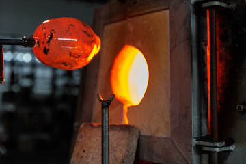 Close-up glassblowing process tube tool with molten glass shaped inside refractory furnace in industrial craft workshop. Handmade blowing glassware design production manufacture Europe
