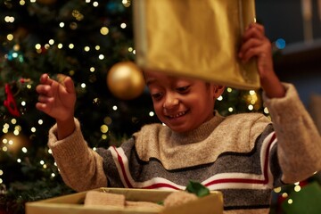 Candid close up portrait of excited African American boy opening presents on Christmas eve and anticipating surprise enjoying magic season copy space