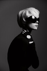 Stylish woman in black attire with futuristic sunglasses, posing confidently against a soft gray background. Modern fashion and elegance concept.