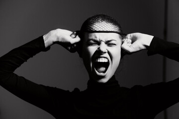 Emotional young woman expressing frustration, wearing a black turtleneck and fishnet headpiece,...