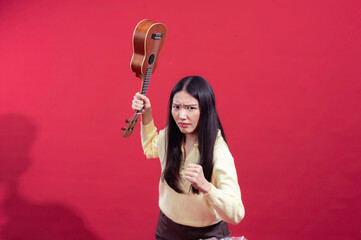 Asian woman holding a ukulele above her head with a determined, intense expression, dressed in a...