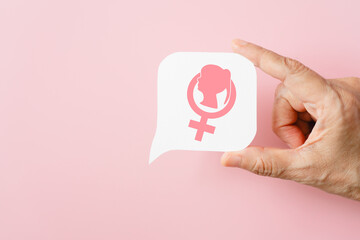 hand hold pink female gender sign with lady icon inside on real white speech bubble paper cut background. For women's power, voice, feminism concept, including copy space