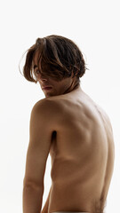 Naklejka premium Portrait of young man posing shirtless and looking at camera over shoulder against white studio background. Male model revealing his bare back. Concept of natural beauty, male health, fashion. Ad