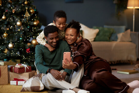 Full length portrait of happy African American family with little boy taking selfie photo via smartphone enjoying cozy Christmas celebration together