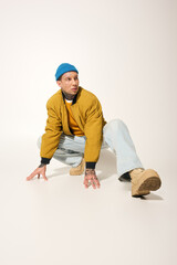 A tattooed young man poses creatively on a light background while wearing casual attire.