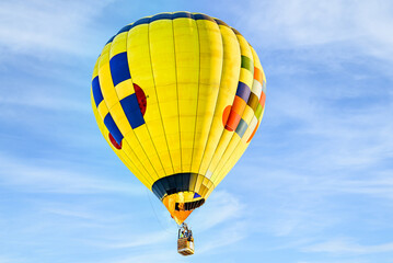 Colorful hot air balloon flying over blue sky with white clouds	