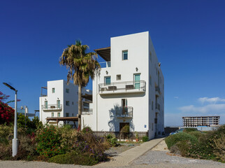 Obraz premium Stunning coastal buildings surrounded by vibrant greenery under a clear blue sky.