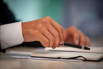 Hands actively involved in a business discussion, diligently taking notes with a pen on a notebook for reference