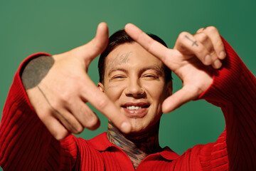 The young man smiles widely, showcasing his tattoos while forming a playful gesture. © LIGHTFIELD STUDIOS