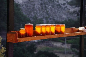 jars of natural bee honey are on the shelf , illuminated by the sun