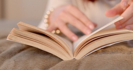 A person is comfortably sitting on a cozy bed while engrossed in reading an interesting book that...