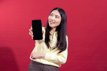 Asian woman smiling while extending a smartphone towards the camera, wearing a yellow sweater...