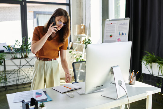 A young non binary person talks on the phone, focused on their modern office setup.
