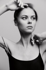 Elegant young woman posing with a thoughtful expression, wearing a black top, against a soft gray...