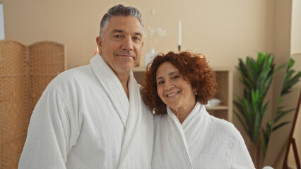 Middle-aged couple in white bathrobes enjoying a relaxing moment together at a spa, embracing wellness and tranquility in an inviting indoor setting