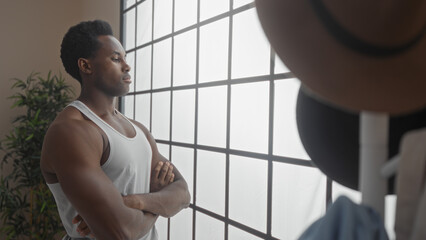 Young man standing in a bedroom looking out a window with arms crossed, reflecting indoors.