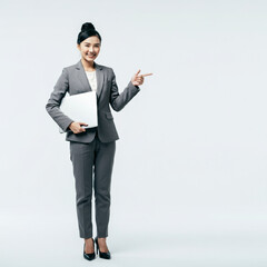 Asian businesswoman holding a laptop while pointing to the copy space beside her on isolated white background