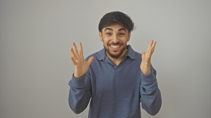 Fototapeta premium Handsome young adult arab man with a beard in casual clothing gestures excitedly against a white background.