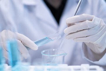 Close-up scientist pouring blue liquid into test tube beaker flask equipment pipette working...