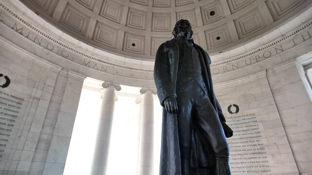 A bronze statue of Thomas Jefferson stands in the interior of the Jefferson Memorial, facing the inscription I Have Sworn Upon The Mind Of, surrounded by white marble walls, Washington DC.