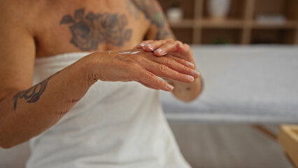 Mature woman receiving a hand massage in an indoor spa, showing detailed tattoos and wearing a towel with a blurred background of a wellness center.