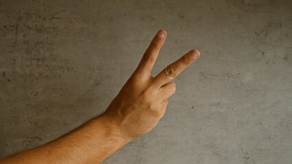 Man's hand showing peace sign with fingers against a concrete background symbolizing victory or...