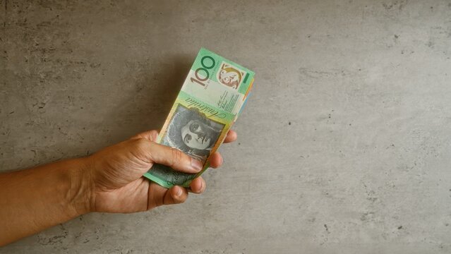 Man holding a stack of australian dollars against a concrete background, emphasizing wealth and finance in australia with close-up focus on the money and hand.