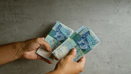 Man holding hong kong dollars against a concrete background, counting money with both hands clearly visible.