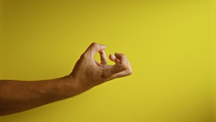 Man's hand forming an ok gesture against a vibrant yellow background, showcasing fingers in relaxed...
