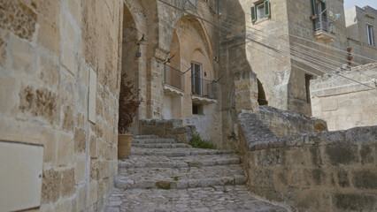 A rustic, outdoor scene in matera, basilicata, italy, showcases historic stone architecture with a rough cobblestone path under a bright, sunny sky in a quiet european town.