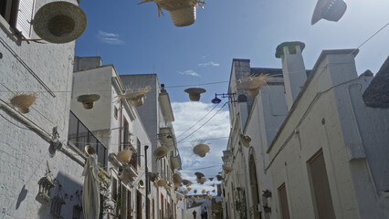 Charming street in alberobello, italy decorated with hanging hats on a sunny day, showcasing the...