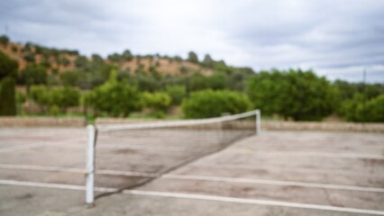 Outdoor tennis court in a defocused setting with lush greenery and hills in the background on a cloudy day creating a serene and natural atmosphere